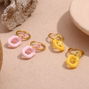 Dettaglio di orecchini in acrilico rosa e giallo con cerchi placcati in oro 18 carati su sabbia