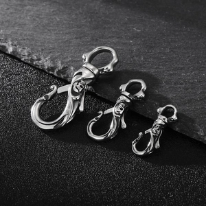 Polished stainless steel skull keychains in three sizes on a textured stone background