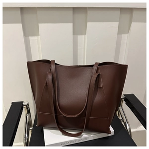 Dettaglio borsa tote in pelle marrone scuro su libri contro una parete bianca