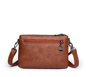 Detail view of brown faux leather crossbody bag with multiple zippers and gunmetal hardware