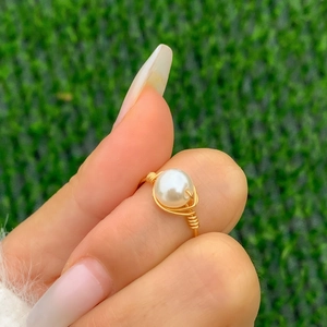 Macro view of a handmade wire-wrapped ring with a glossy white pearl on a gold band