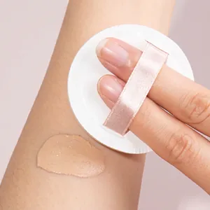 Round cream cushion puff with pink ribbon showing makeup blending effect on arm