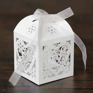 Macro shot of white laser-cut heart candy box with satin ribbon on wood background