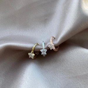 Close-up of gold, silver, and rose gold hoop earrings with star-shaped crystals on satin