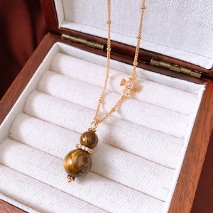 Close-up of tiger eye gourd pendant necklace with zircon detail on vintage wooden box
