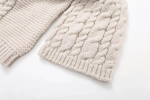 Detailed macro view of beige knitted sweater showing cable stitch patterns and ribbed cuffs