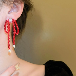 Detail of elegant red beaded bow earrings with white faux pearl drop on model