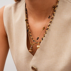 Détail d'un collier multicouche en œil de tigre avec cœurs dorés et pendentifs gourde