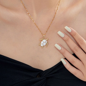 Close-up of a gold turtle pendant necklace with white inlay worn by a model