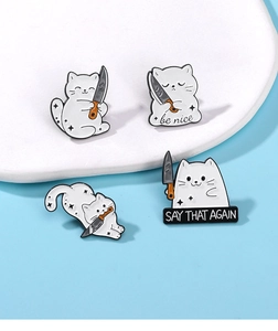 Detail of four funny white cat enamel pins with knives and slogans on a tray