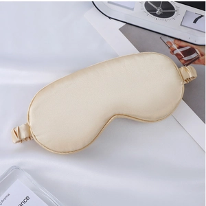 Close-up of champagne silk sleep mask on white fabric with cozy bedroom decor