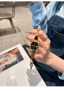 Elegant gold chain watch with black square dial worn on wrist in a cafe setting