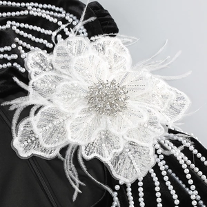 Détail de fleur en dentelle blanche avec perles et plumes sur robe en velours noir