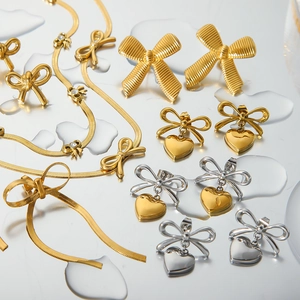 Artistic layout of gold and silver bow earrings with heart pendants on a reflective surface
