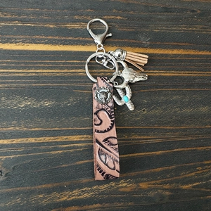Détail d'un porte-clés en cuir avec pendentif tête de taureau, cactus et pompon sur bois