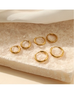 Close-up of three pairs of polished gold hoop earrings on marble stone background