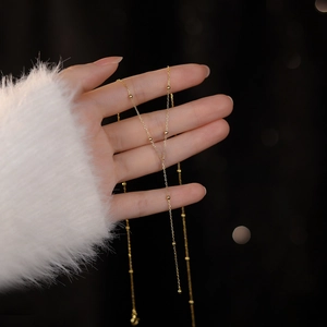 Elegant S925 sterling silver gold beaded tassel necklace held against a bokeh background