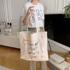 Detailed view of cream canvas tote bag featuring graffiti letter print in a modern setting