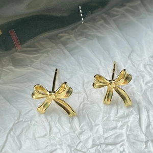 Macro shot of 18k gold plated S925 silver bow earrings on white textured background