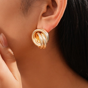 Detail of twisted gold geometric hoop earrings on model with textured metallic finish