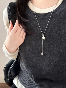 Detail of silver star Y-shaped necklace on model with layered knitwear and white shirt
