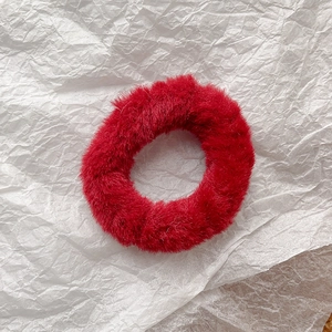 Close-up of red faux rabbit fur elastic hair tie with soft plush texture on white background