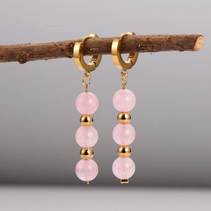 Handmade gold hoop earrings with three pink crystal beads on a natural wooden branch