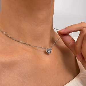 Close-up of a silver heart necklace with a large crystal center worn by a female model