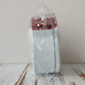 Detail of a rectangular tin candy box with red and black plaid lid in plastic packaging