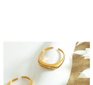 Close-up of two polished gold signet rings with adjustable open band design on white surface