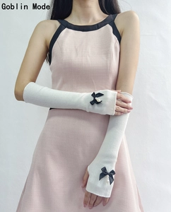 Detail of white knit arm sleeves featuring a black bow and pearl accent on a model