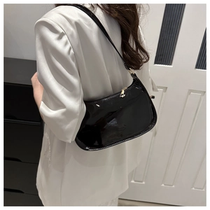 Close-up of a small black patent leather baguette shoulder bag worn by a model
