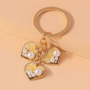 Detail of golden heart-shaped pendants with white pearls and yellow enamel on a keychain