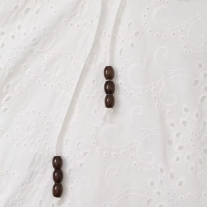 White halter dress featuring hollow embroidery details and dark brown wooden beads