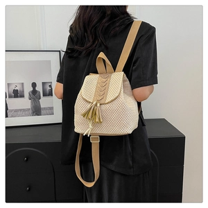 Detail of a beige straw backpack featuring brown leather trim and stylish tassel accents