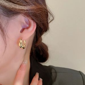 Gros plan de boucles d'oreilles créoles dorées en forme de C portées par un mannequin