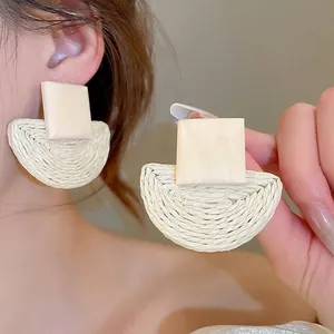 Close-up of bohemian rattan earrings featuring square studs and half-moon woven pendants