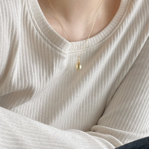 Detail of a minimalist gold teardrop pendant necklace worn on a ribbed knit sweater