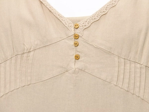 Détail de la dentelle du col en V et des boutons bruns sur la robe midi en lin