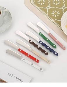 Set of seven stainless steel butter knives with colorful rivet handles on white surface