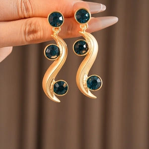 Close-up of wavy gold earrings with dark blue gems worn by a model in soft lighting