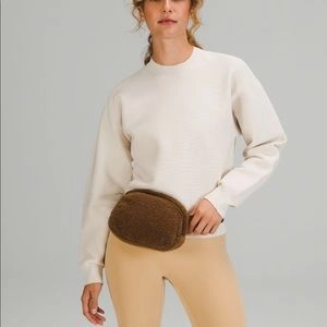 Detail view of the brown plush waist bag worn by a model in a professional studio setting