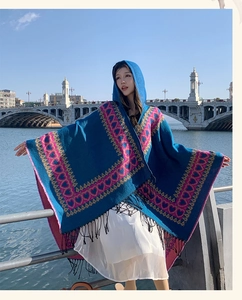 Woman wearing ethnic blue hooded poncho with pink heart pattern against scenic bridge