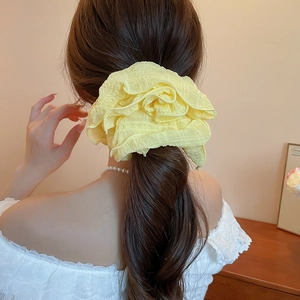 Detail view of a soft yellow ruffled fabric scrunchie on a ponytail hair style