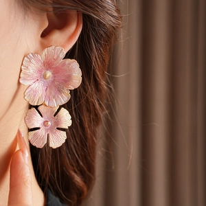 Detail of pink and gold floral earrings with textured petals on a model's ear