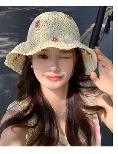 Detailed strawberry embroidery on a beige woven straw bucket hat with natural sunlit shadows