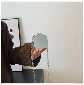 Close-up of mini silver mirror chain bag held by model showing its compact size and gloss