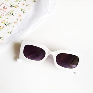 Detail view of white rectangle sunglasses with dark lenses on a clean aesthetic background