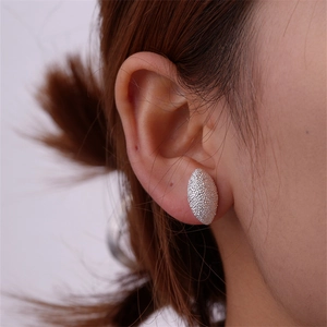Close-up of silver teardrop stud earrings with frosted texture worn by a model