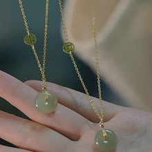 Detail of a gold layering necklace with a green jade pendant and Chinese fortune charms